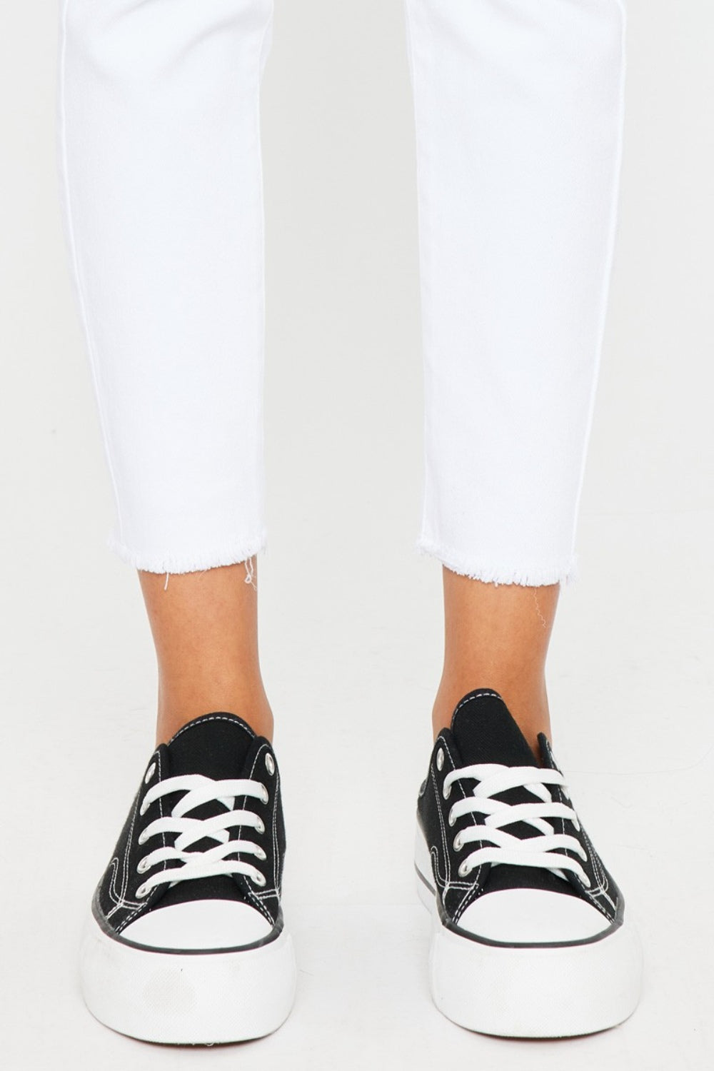 A person models a versatile gray long-sleeve top paired with flattering fit Kancan Mid Rise Ankle Skinny Jeans and sleek black sneakers, all set against a pristine white background.