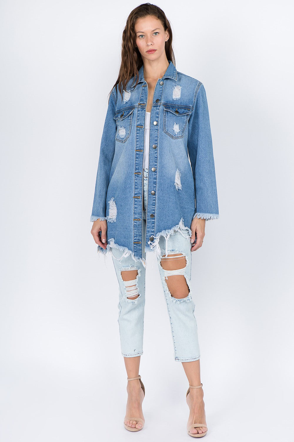 A woman models the American Bazi Distressed Frayed Hem Denim Jacket, featuring frayed edges, a button-up front, and chest pockets that add to its vintage feel. She has long hair and is looking downward with one hand touching her head.