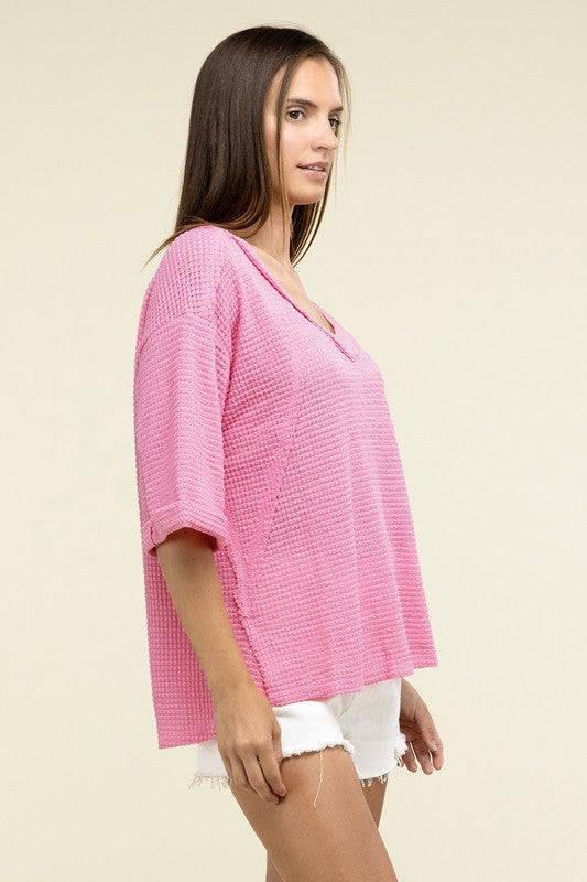 A person is dressed in a Brushed Waffle Exposed-Seam 3/4 Sleeve Top and white shorts, perfect for a casual wardrobe. They stand against a plain background, effortlessly embodying relaxed style.