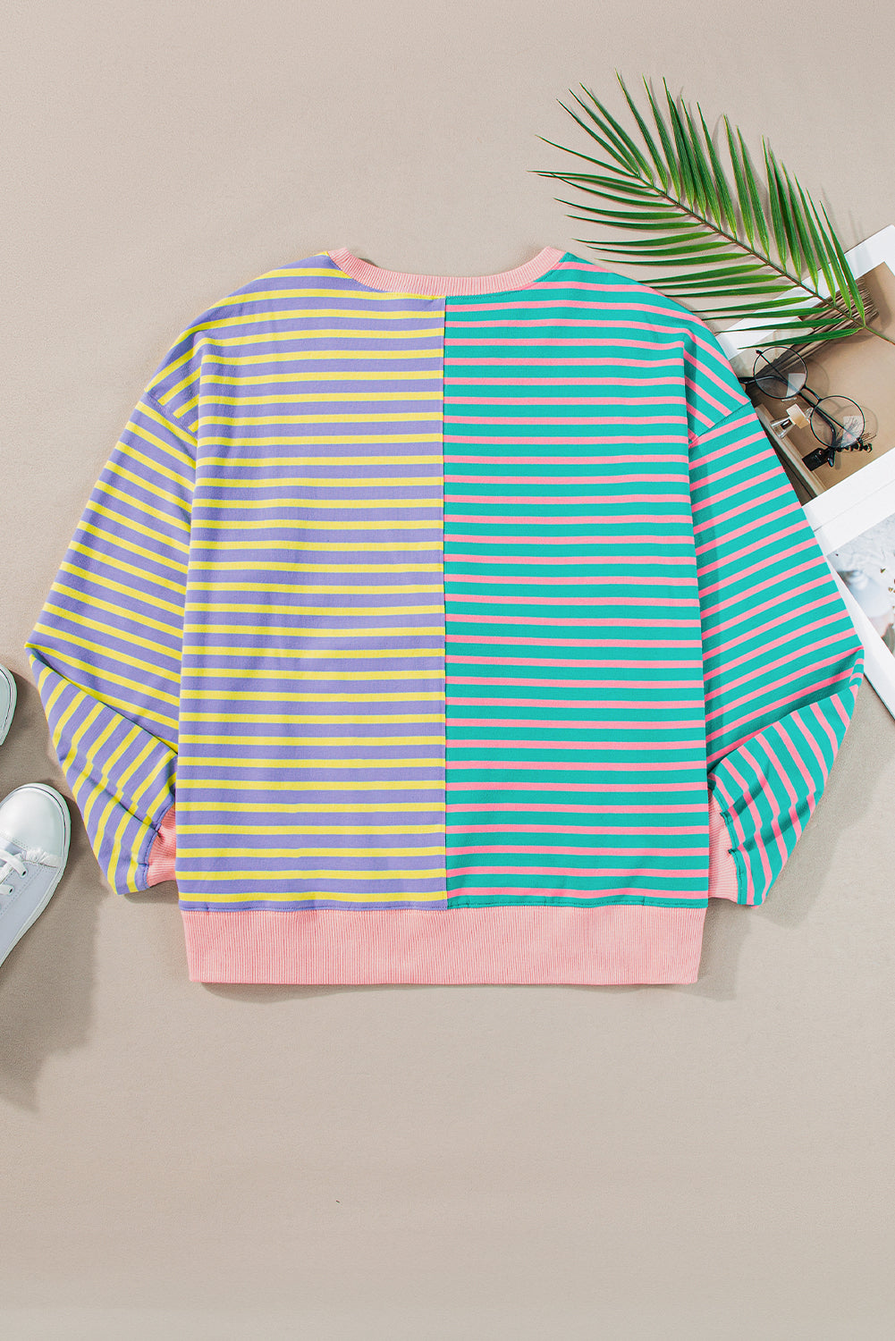 A person with wavy hair is seen from behind wearing a Casual Stripe Colorblock Drop Shoulder Oversize Sweatshirt in pastel colors and blue jeans. They are carrying a white shoulder bag, showcasing a trendy color block design.