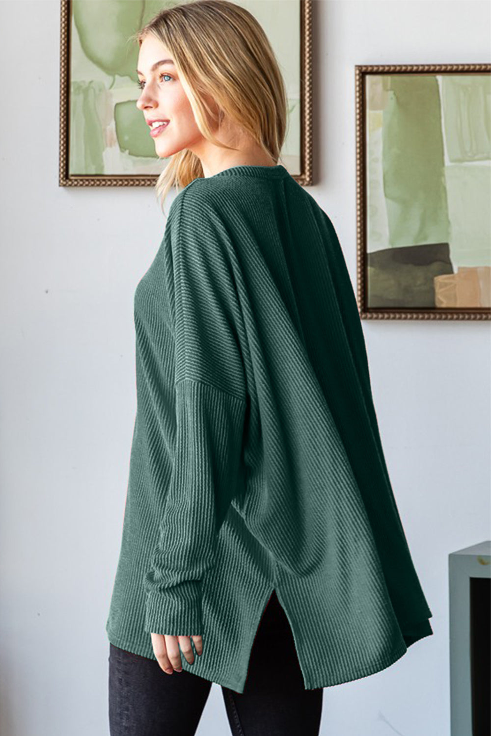 A woman wearing the Heimish Sequin Nutcracker Long Sleeve Ribbed Top smiles while posing indoors, showcasing one of the season's charming holiday outfits.