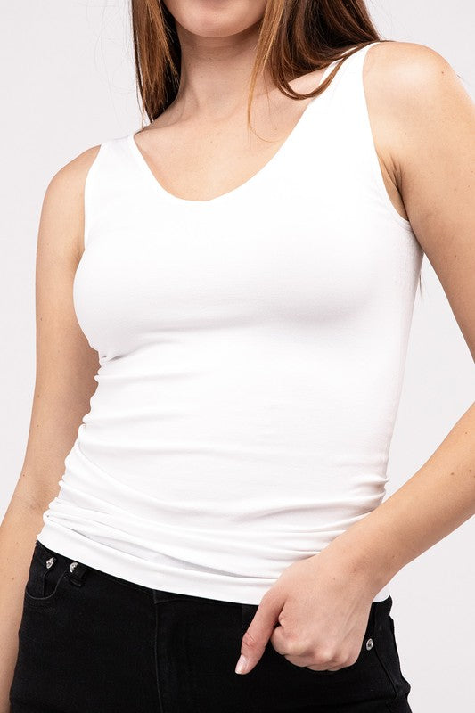 A woman in a white Front & Back 2-Way V-Neck Seamless Tank and black pants, standing with hands on hips and looking at the camera.