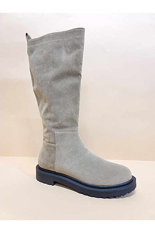 Three pairs of UNA-LONG BOOTS in beige, grey, and black are aligned in a row against a neutral background. These casual suede long boots feature chunky rubber soles and block heels.