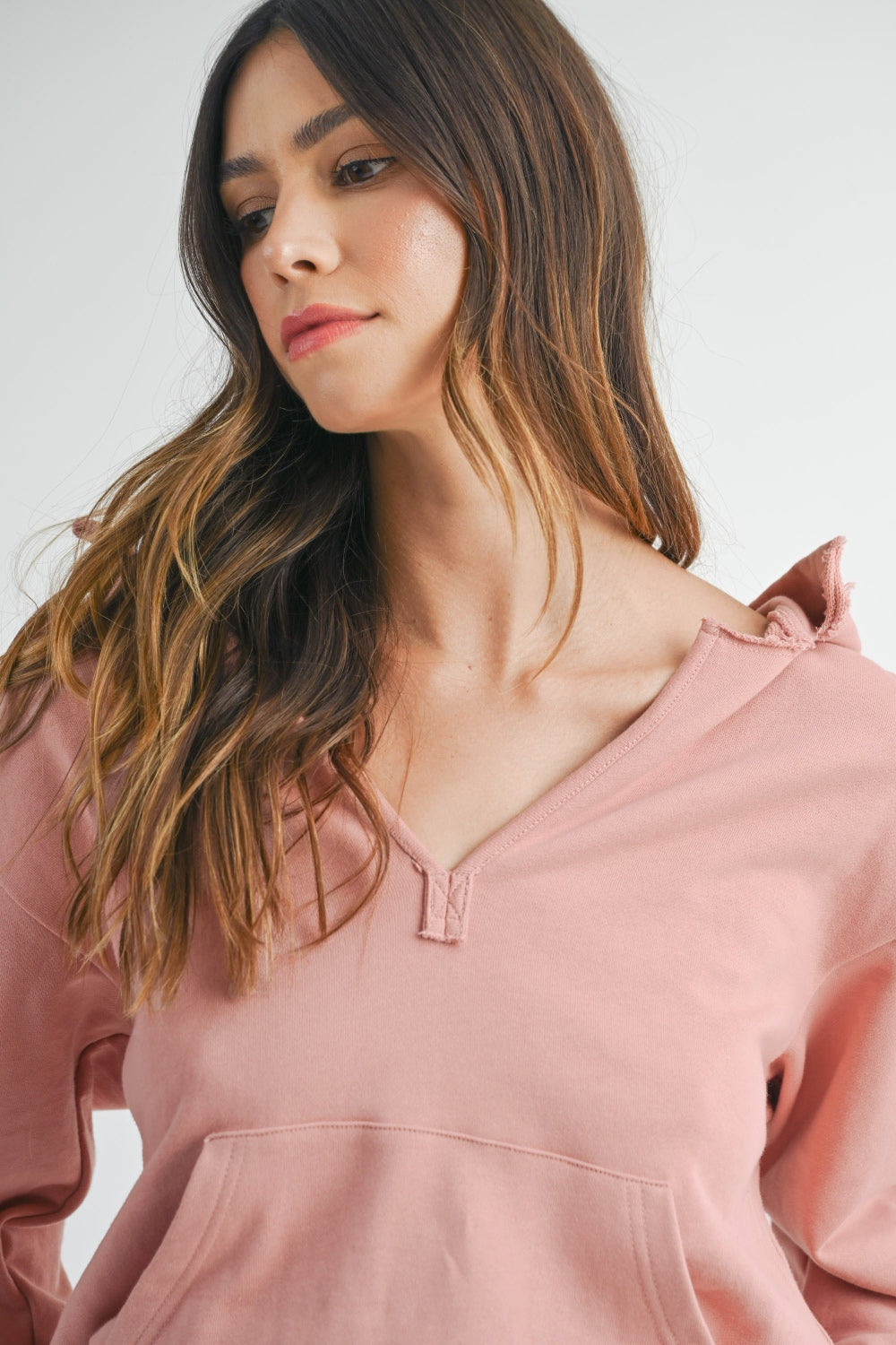 Woman wearing a MABLE French Terry Hooded Romper in pink, hands in pockets, looking directly at the camera.