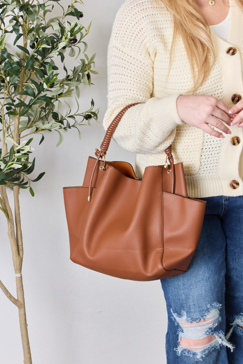 Effortlessly displaying the SHOMICO Faux Leather Handbag with Pouch, which features a spacious design in brown with gold accents and a woven handle, this piece exemplifies versatility. Paired with a cream sweater and blue jeans, its minimalist style perfectly balances fashion and function.