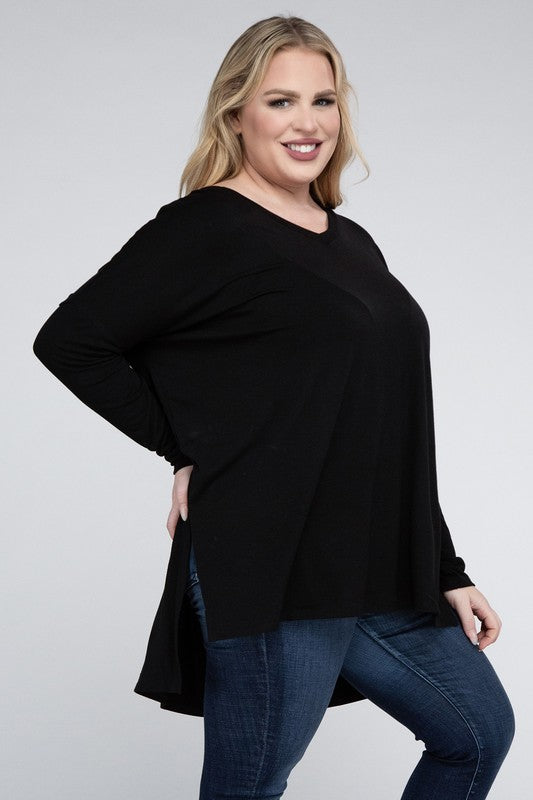 A woman with long, blonde hair wears a Plus Dolman Sleeve V-Neck Side Slit Hi-Low Hem Top and blue jeans, posing with one hand on her hip and smiling at the camera.