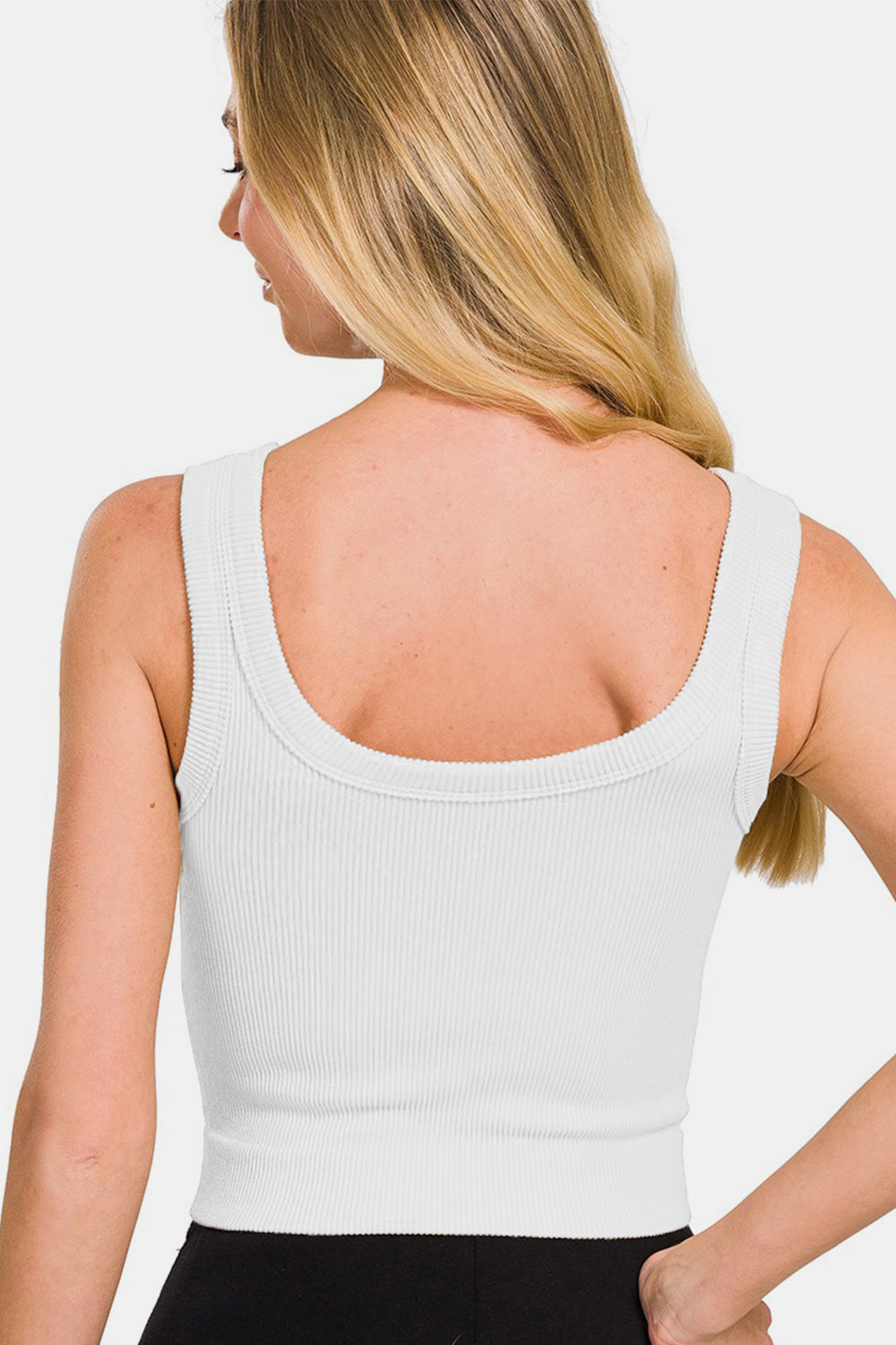 A person with long hair wearing a white Zenana Ribbed Round Neck Cropped Tank and black pants.