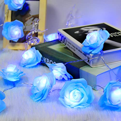 The Blue Rose Flower String Lights - 14.7ft 30 LED Fairy Lights Flower Garland Lights are elegantly draped over a stack of books and a framed photo, creating a romantic, glowing decor for any occasion, whether it's indoors or outdoors.