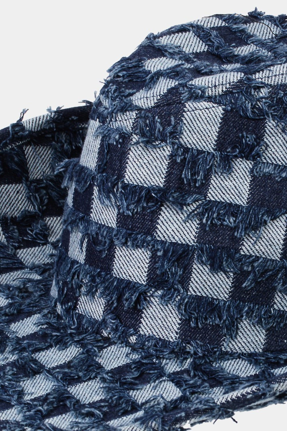 The Fame Checkered Fringe Denim Cowboy Hat, featuring a wide brim and adorned with a blue checkered pattern along with frayed denim edges, rests on a pristine white surface. It includes an adjustable inner string and a matching blue chin strap for added style and functionality.