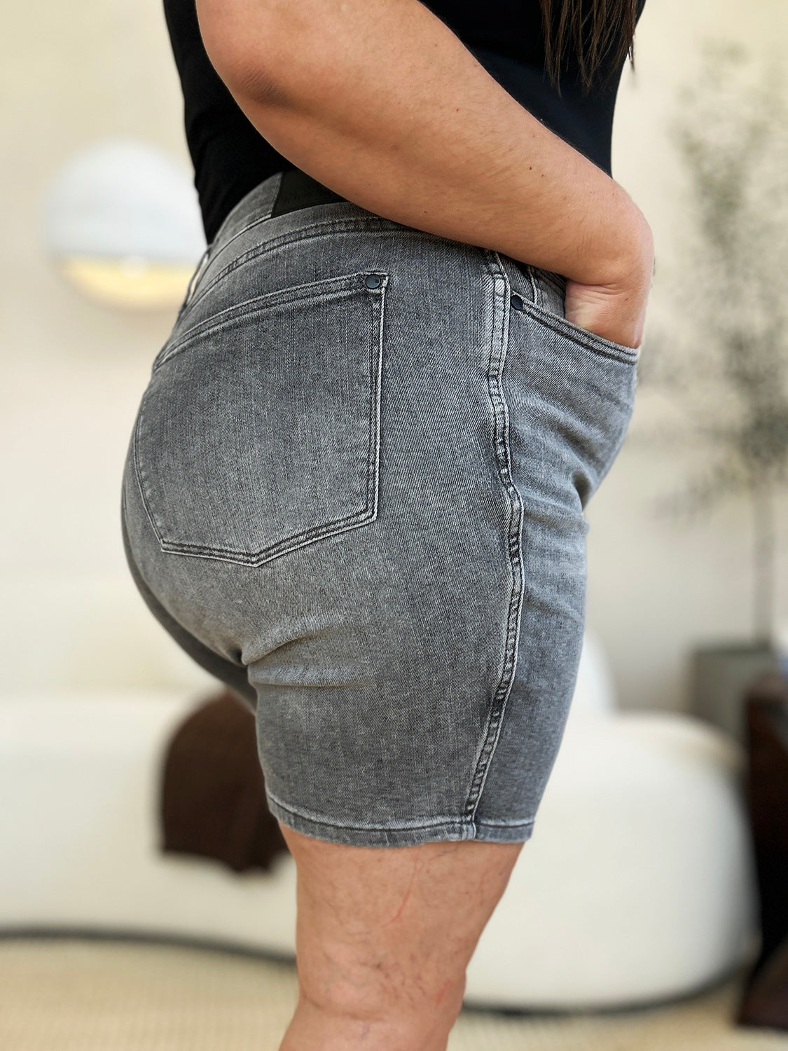 A person wearing a white top and the Judy Blue Full Size High Waist Washed Denim Shorts with vintage charm has one hand in their pocket. The shorts, featuring a faded design and belt loops, contribute to a retro-inspired look.