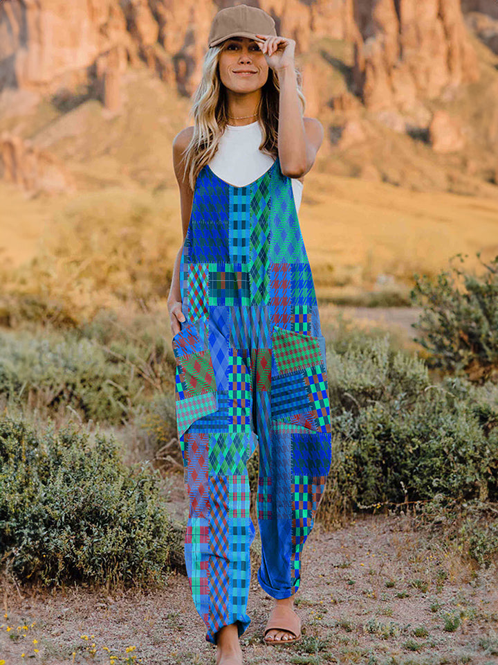 A woman stands outdoors in front of a rocky landscape, wearing the Full Size Printed V-Neck Sleeveless Jumpsuit and a brown brimmed hat. She is smiling and holding the brim of her hat with one hand, exuding the carefree vibe of this vibrant and colorful jumpsuit.