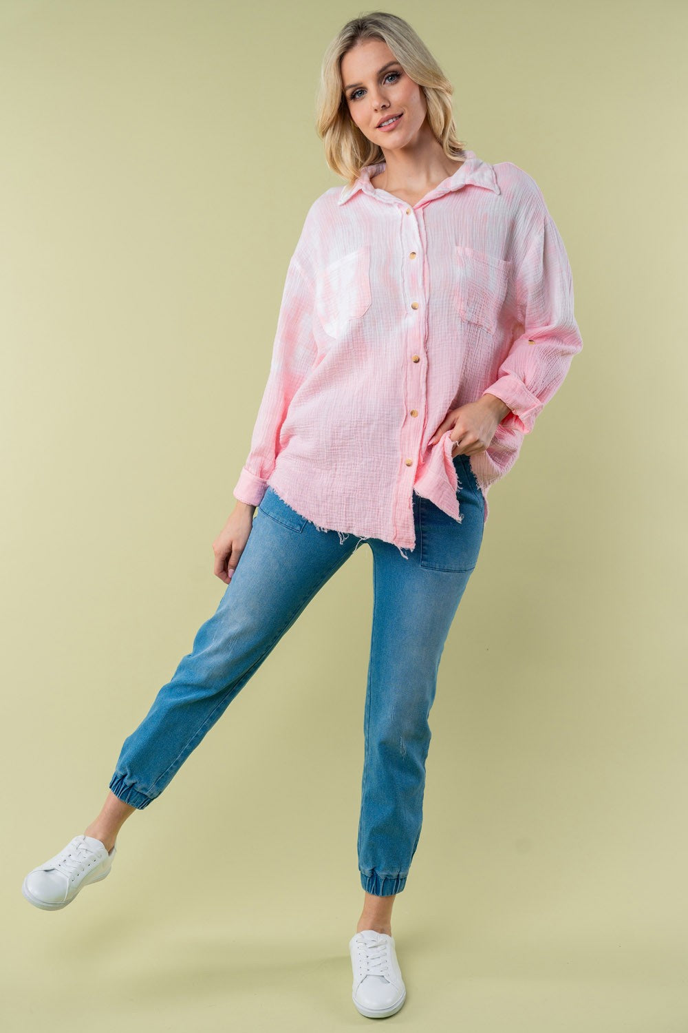 A person wearing the White Birch Full Size Long Sleeve Tie Dye Shirt with rolled-up sleeves stands against a plain background, holding a strand of their hair with one hand.