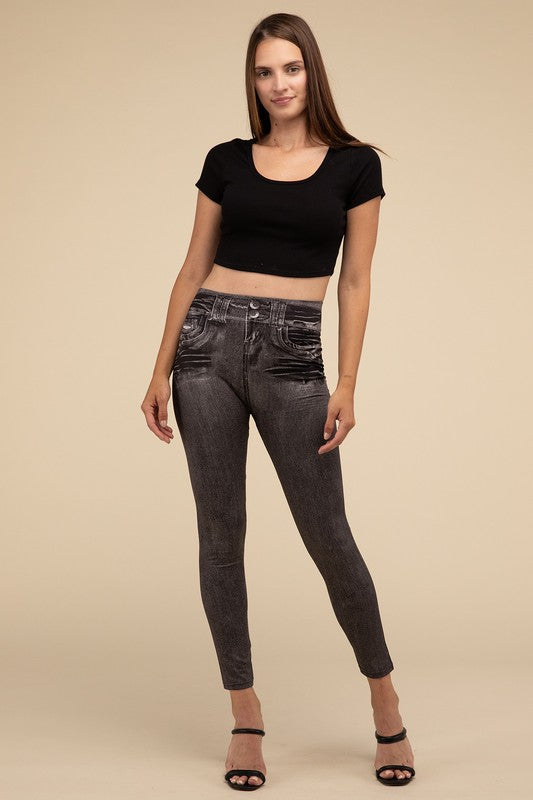 A person wearing Denim Leggings in a high-waisted black design and paired with black heels poses against a plain beige background, highlighting the sleek, stretchy fit.