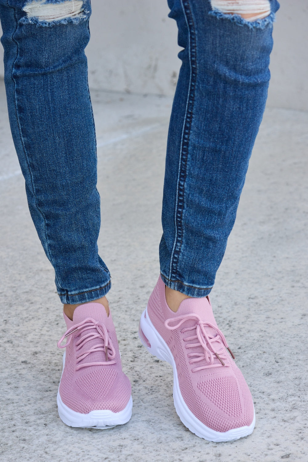 A person is wearing ripped blue jeans and Forever Link breathable mesh lace-up round toe athletic shoes, standing on a concrete surface.