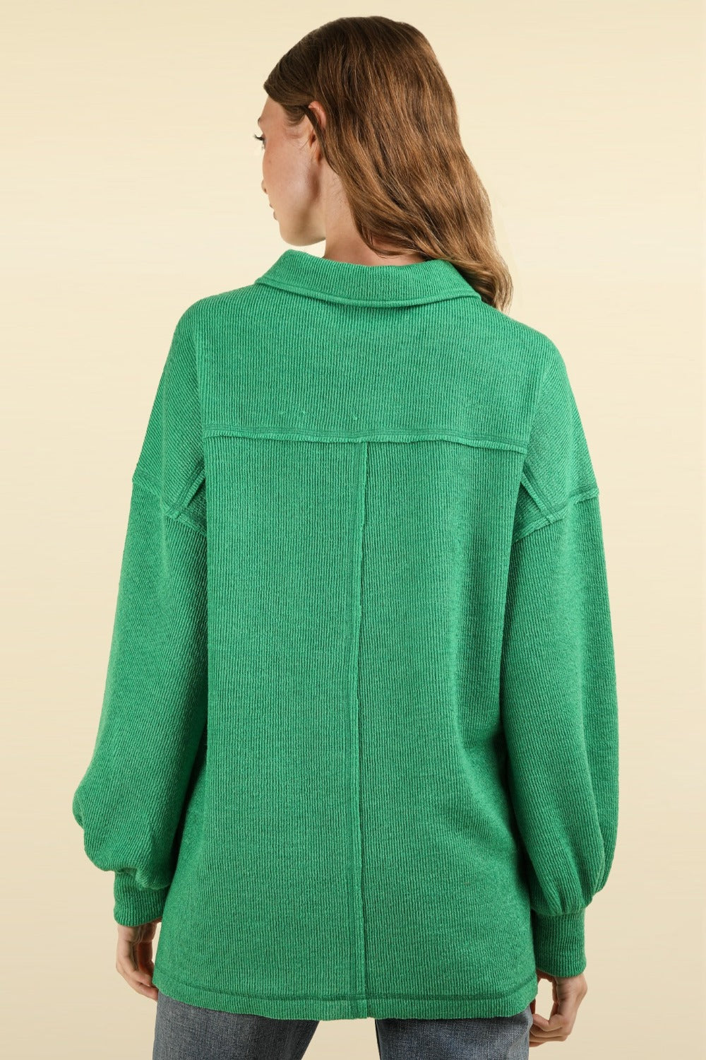 A person with long hair wearing an oversized fit, green VERY J Collared Half Button Knit Top with Pockets stands against a beige background.