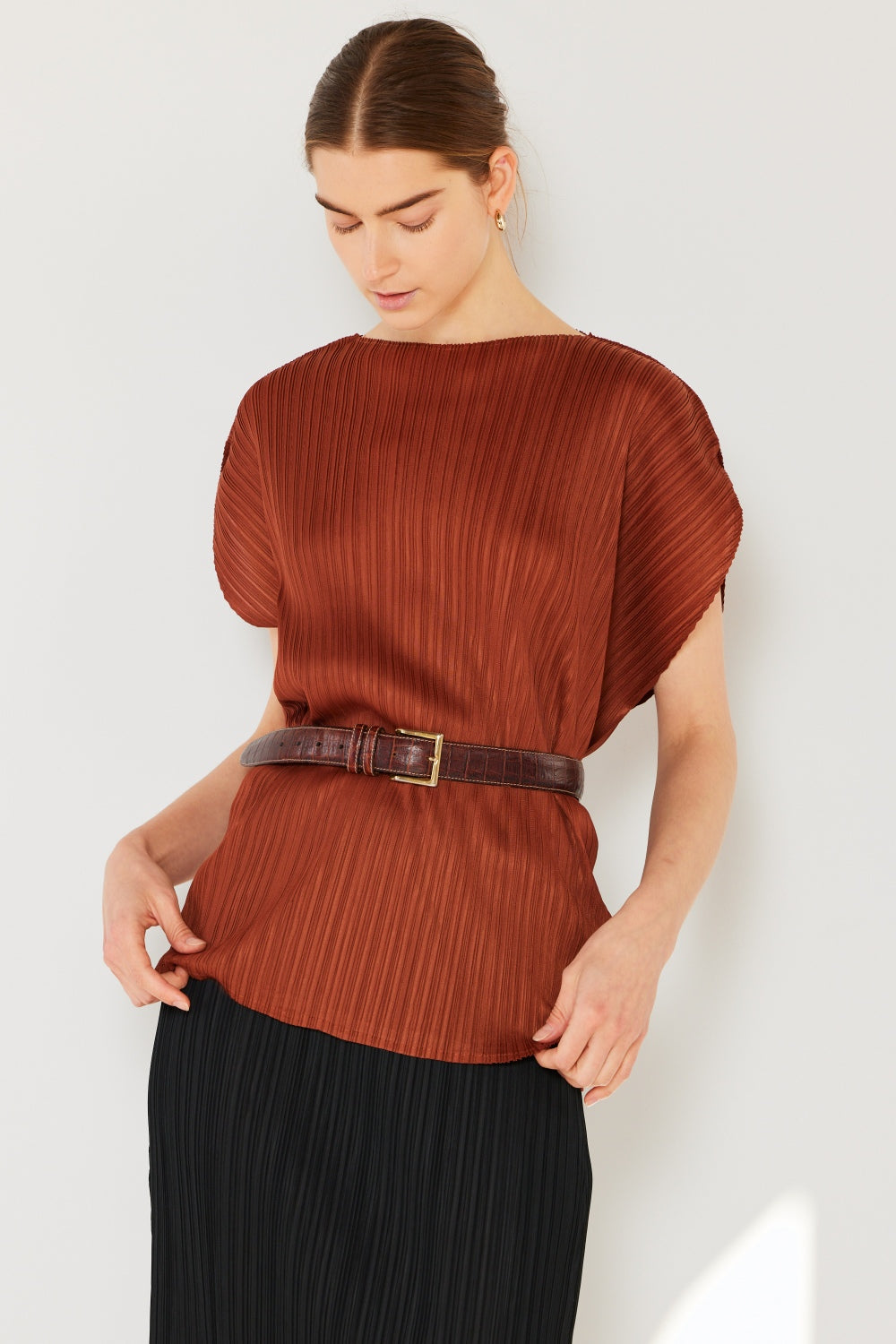 A person wearing the Marina West Swim Rib Pleated Oversized Dolman Sleeve Top in a fashionable light blue shade, paired with a brown belt and black skirt, stands against a plain background.