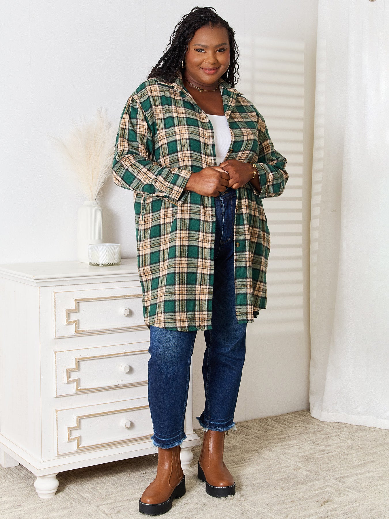 A person wearing the Mandy Plaid Collared Neck Long Sleeve Shirt in green and beige over a white crop top and blue jeans, standing indoors near a white dresser with vases.