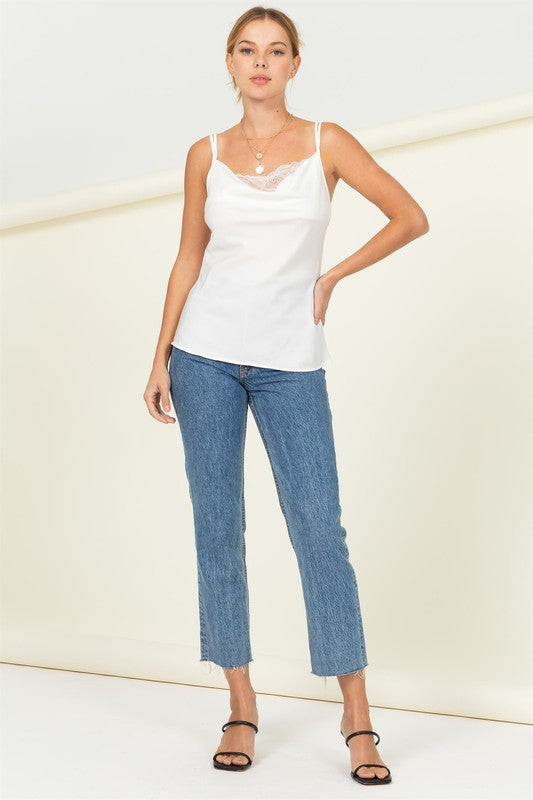 A person is standing in front of a light background, wearing the Two Strap Cami with Lace Top paired with blue jeans.