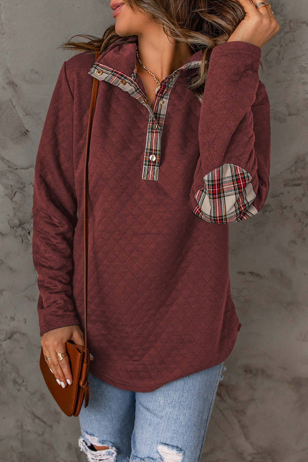 A person with wavy hair is wearing a chic Fiery Red Geometric Texture Plaid Trim Sweatshirt. They have a brown crossbody bag and are facing away from the camera, with a gray textured wall in the background.