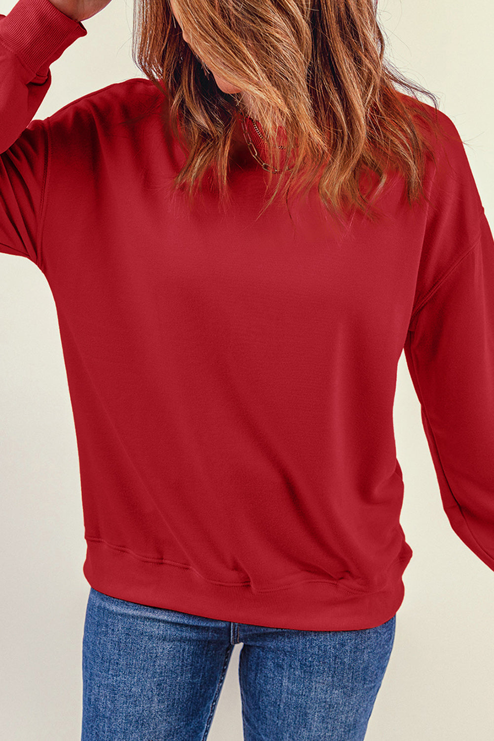 A person wearing a long-sleeved red shirt and blue jeans stands with their back to the camera, one hand resting on their hip, as if showcasing a cozy Fiery Red Plain Crew Neck Pullover Sweatshirt for winter.