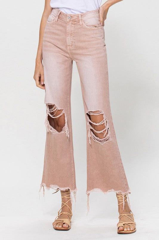 Person wearing 90's Vintage Crop Flare Jeans in rose pink with high waist, distressed details, rips on the knees, and frayed hems, paired with beige strappy sandals.