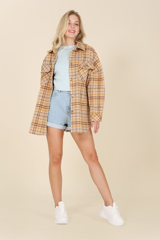 A person wearing the beige and brown Plaid shacket with pockets, featuring long sleeves and large buttons, holds the collar. Blonde hair is visible, adding a touch of elegance to the casual look.