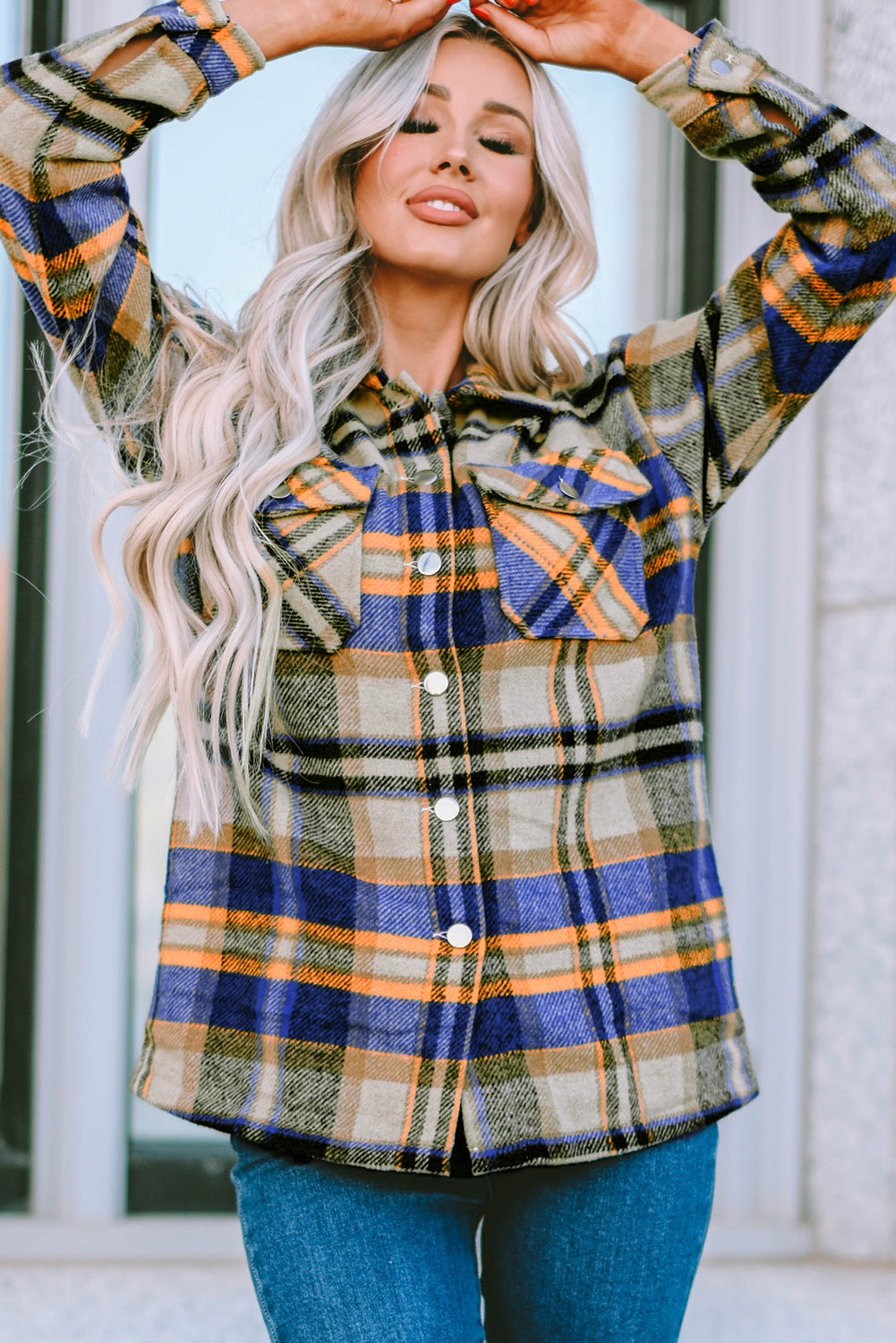 A person wearing a Brown Plaid Button Up Long Sleeve Flannel Shacket layered over a white top with ripped jeans and holding a brown handbag stands against a textured gray wall.