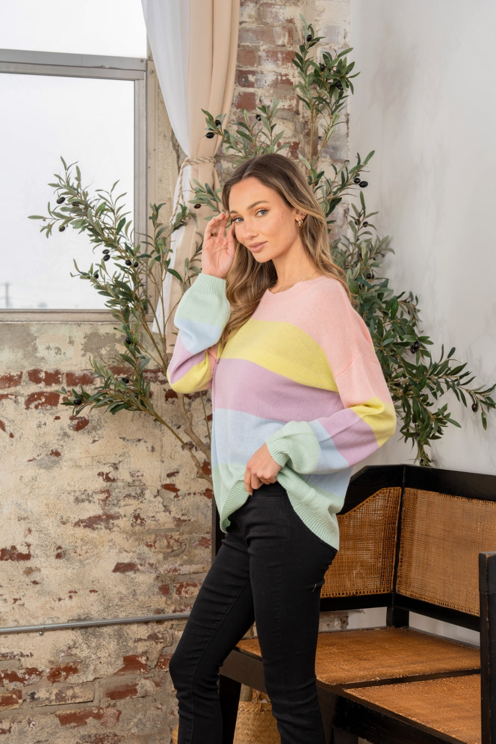 A woman wearing the Sew In Love Full Size Color Block Round Neck Dropped Shoulder Sweater stands indoors next to a chair and potted plant.