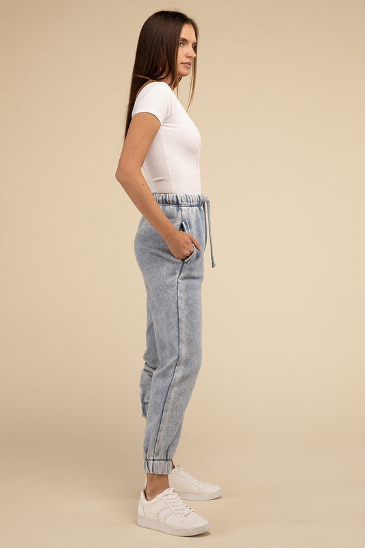 Woman in a white tank top and Acid Wash Fleece Sweatpants with Pockets, standing against a beige background, only showing from the waist down.