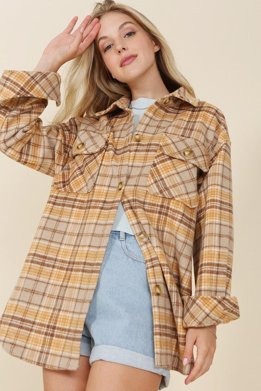 A person wearing the beige and brown Plaid shacket with pockets, featuring long sleeves and large buttons, holds the collar. Blonde hair is visible, adding a touch of elegance to the casual look.