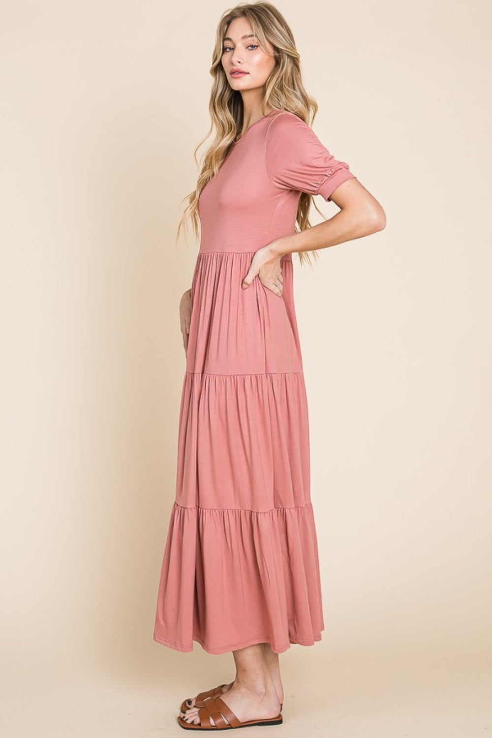 A person wearing the BOMBOM Short Sleeve Tiered Maxi Dress in pink, showcasing its comfortable style with a long, tiered design, stands against a beige background.