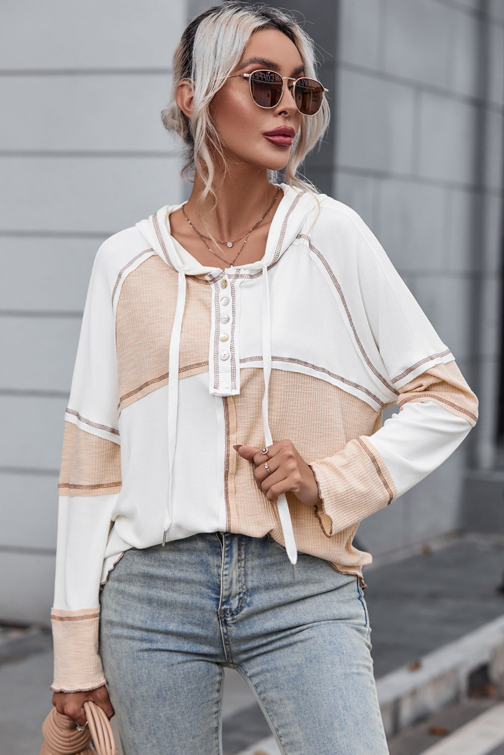 A person with light blonde hair in a bun, wearing sunglasses and a Multicolor Colorblock Seamed Ribbed Henley Hoodie, is walking outside on a paved street.