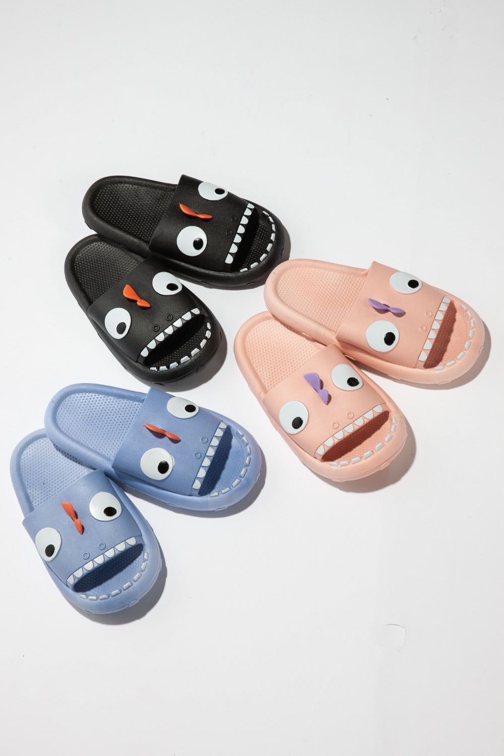 The NOOK JOI Monster Pillow Cloud Slides Non-Slip Slipper features cartoonish monster faces with large eyes, a purple nose, and an open mouth with teeth. Made of durable EVA material, these fun pink cloud slippers also boast an anti-slip design for added safety.