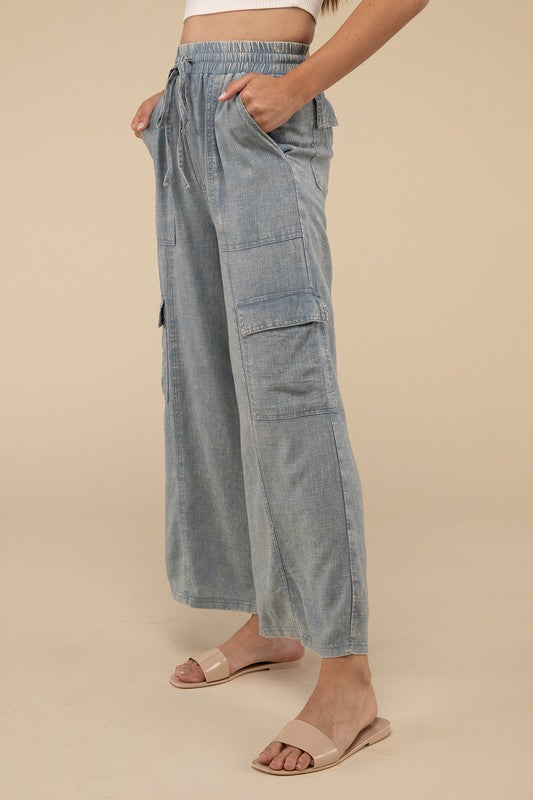 A person wearing Washed Linen Elastic Band Waist Cargo Pants in light blue with hands in pockets, paired with a white top and open-toe sandals. The background is plain beige.