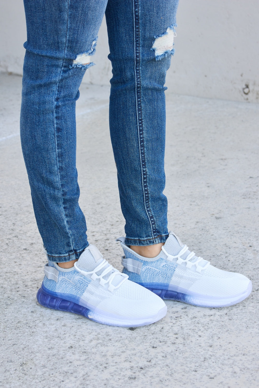 A person wearing distressed blue jeans and a pair of Forever Link Gradient Lace-Up Mesh Breathable Athletic Shoes, standing on a concrete surface.