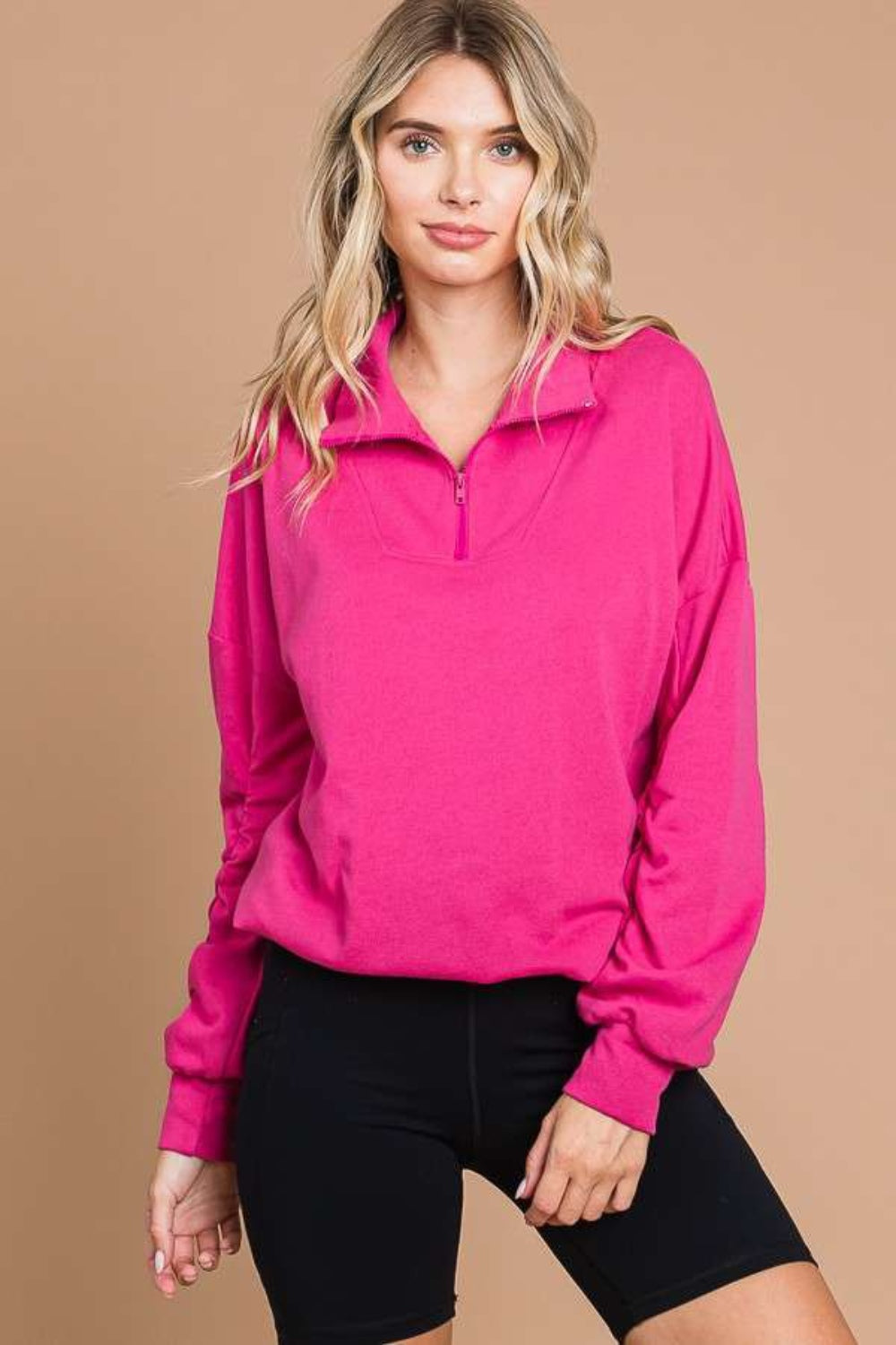 Person wearing a bright pink Culture Code Full Size Half Zip Long Sleeve Sweatshirt and black shorts, standing against a beige background.