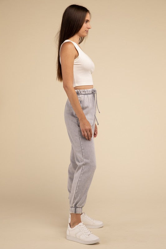 Woman in a white tank top and Acid Wash Fleece Sweatpants with Pockets, standing against a beige background, only showing from the waist down.