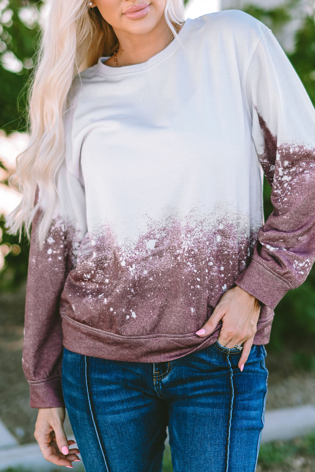 A person with long blonde hair is standing outdoors, facing away from the camera, wearing a Tie Dye Gradient Pullover Sweatshirt featuring a white and brown ombre splatter design.