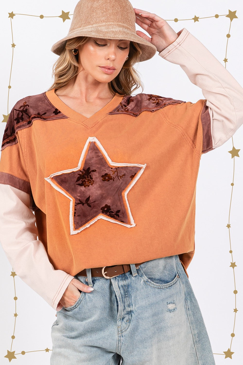 A person wearing a beige hat, a SAGE + FIG Star Patch Long Sleeve Color Block T-Shirt in orange, and light blue jeans stands against a plain background.
