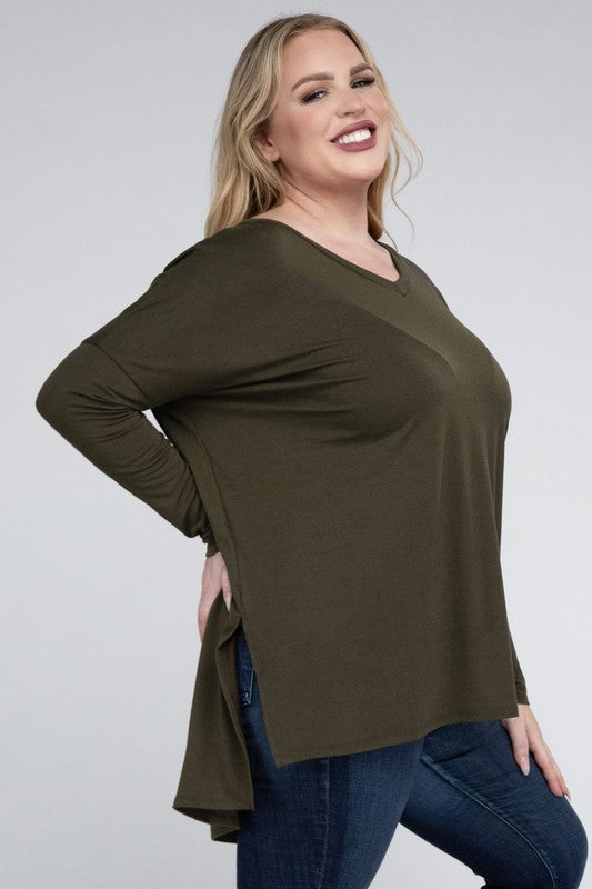 A woman with long, blonde hair wears a Plus Dolman Sleeve V-Neck Side Slit Hi-Low Hem Top and blue jeans, posing with one hand on her hip and smiling at the camera.