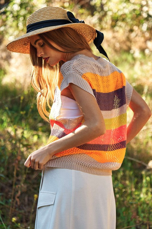 A woman outdoors wearing a Crochet Multi Striped Pullover Knit Sweater Vest and white pants, with her arms raised and eyes closed.