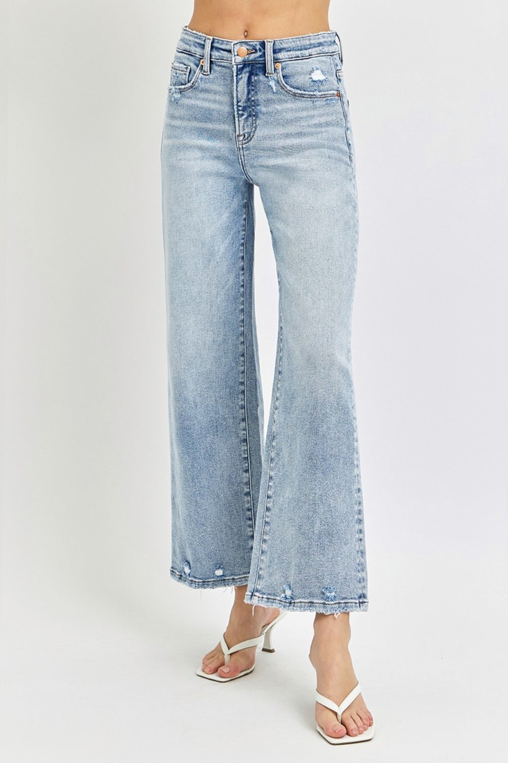 A person wearing RISEN Full Size Tummy Control High Rise Crop Wide Leg Jeans in a light-wash with a frayed hem and white open-toe sandals.