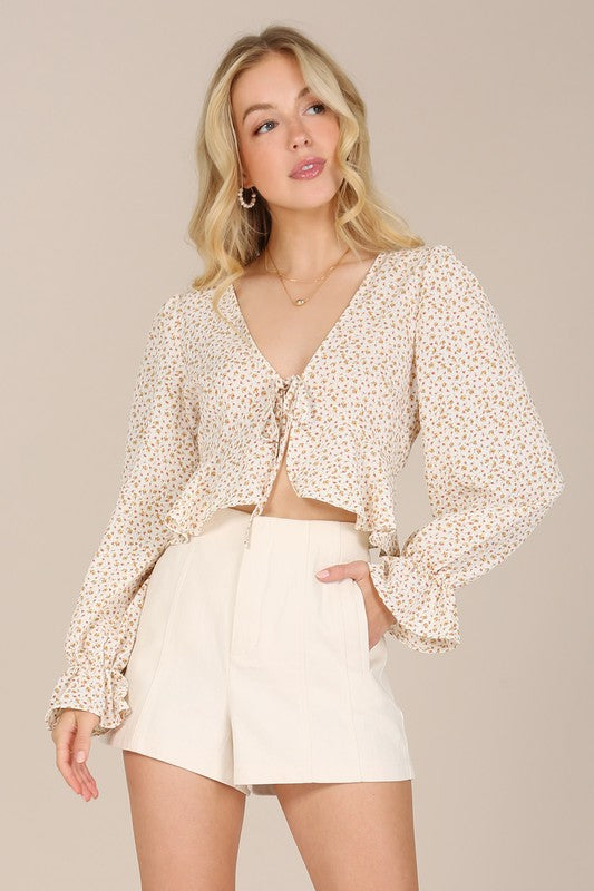 A person wearing an LS floral frill blouse with puff sleeves and beige shorts poses against a neutral background.