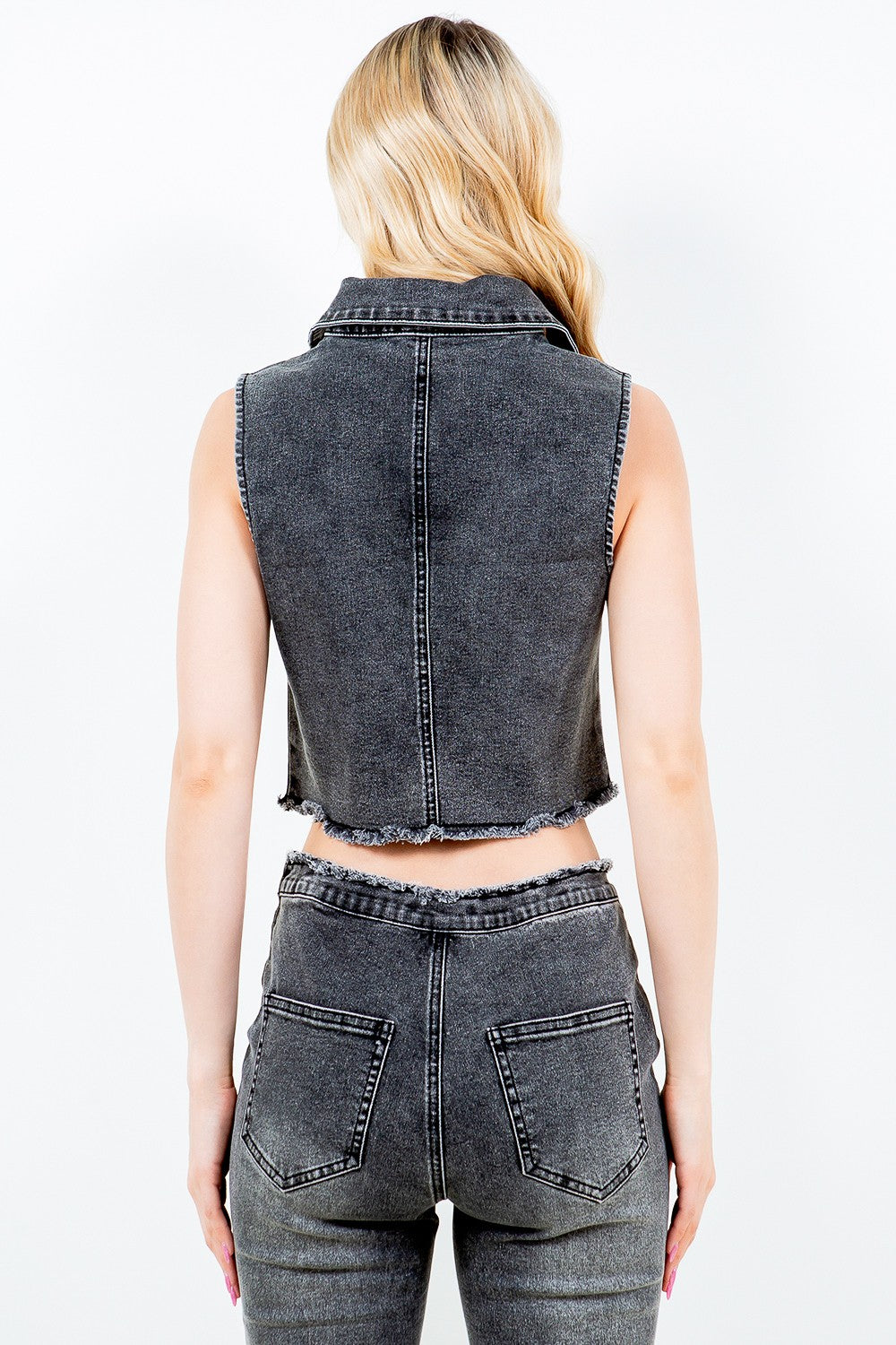 A woman with long, wavy blonde hair is wearing the American Bazi Zip Up Washed Crop Denim Vest and matching high-waisted pants. She stands against a plain white background.