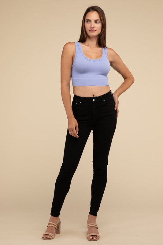 A person with long brown hair wearing the Ribbed Seamless Crop Top in light blue and black pants stands against a beige background, showcasing a perfect summer essential.