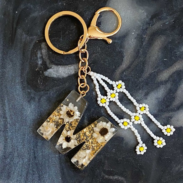 Baby Daisy Initial Key Chain alphabet keychains with real daisy flowers and gold flakes on a marble surface.