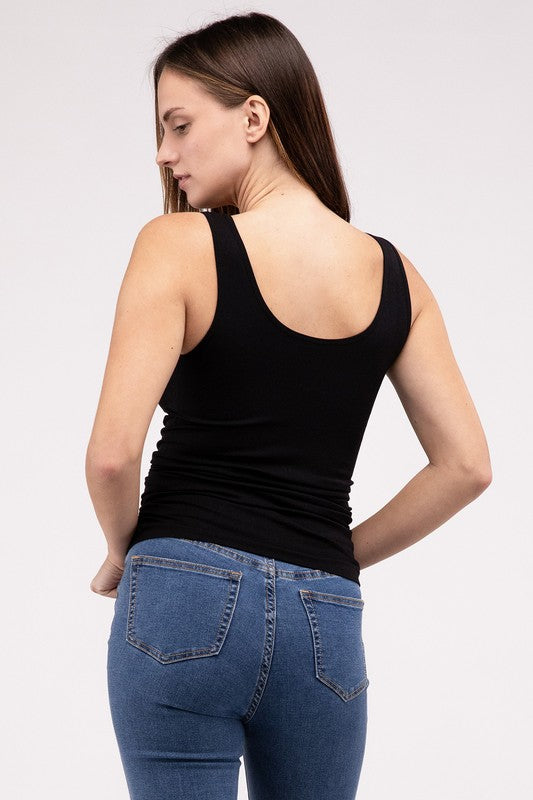 A woman in a white Front & Back 2-Way V-Neck Seamless Tank and black pants, standing with hands on hips and looking at the camera.