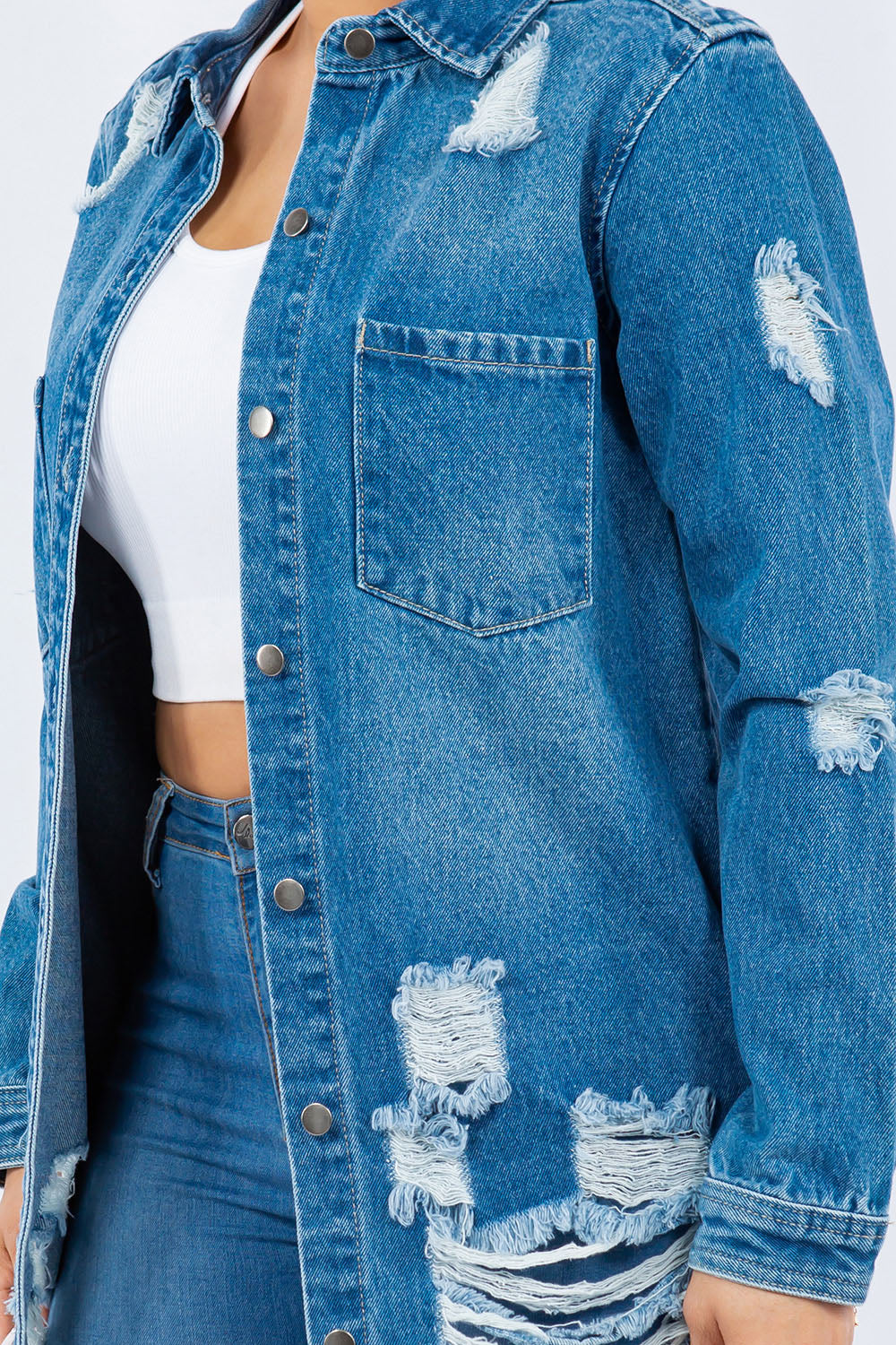 Woman wearing an American Bazi Distressed Button Up Long Sleeve Denim Jacket over a white crop top and blue jeans, standing against a plain background.