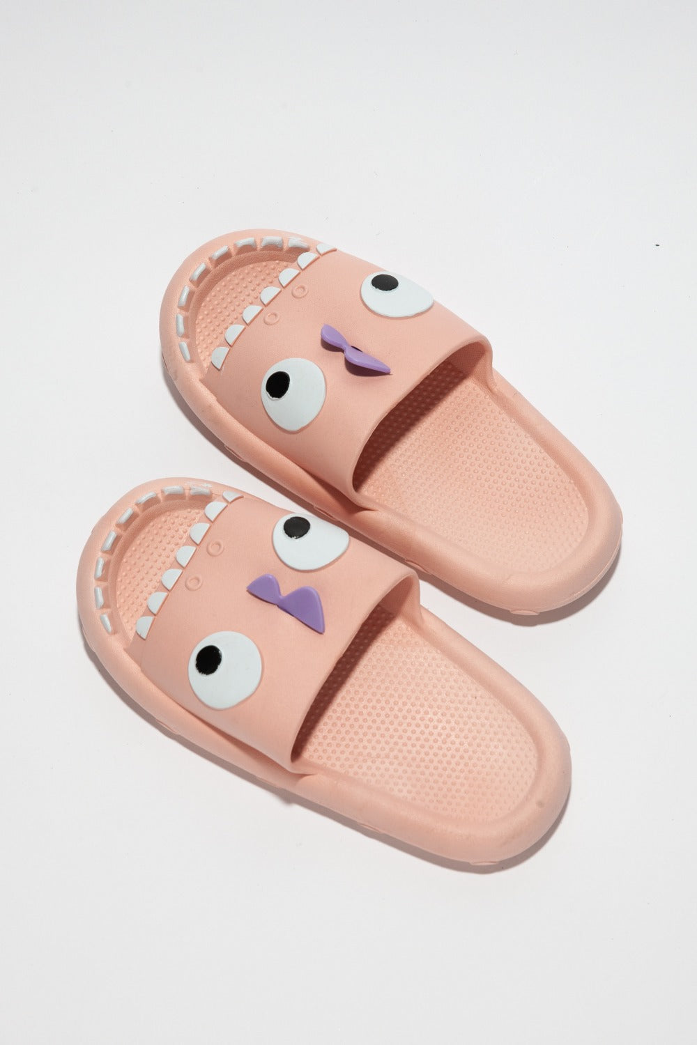 The NOOK JOI Monster Pillow Cloud Slides Non-Slip Slipper features cartoonish monster faces with large eyes, a purple nose, and an open mouth with teeth. Made of durable EVA material, these fun pink cloud slippers also boast an anti-slip design for added safety.