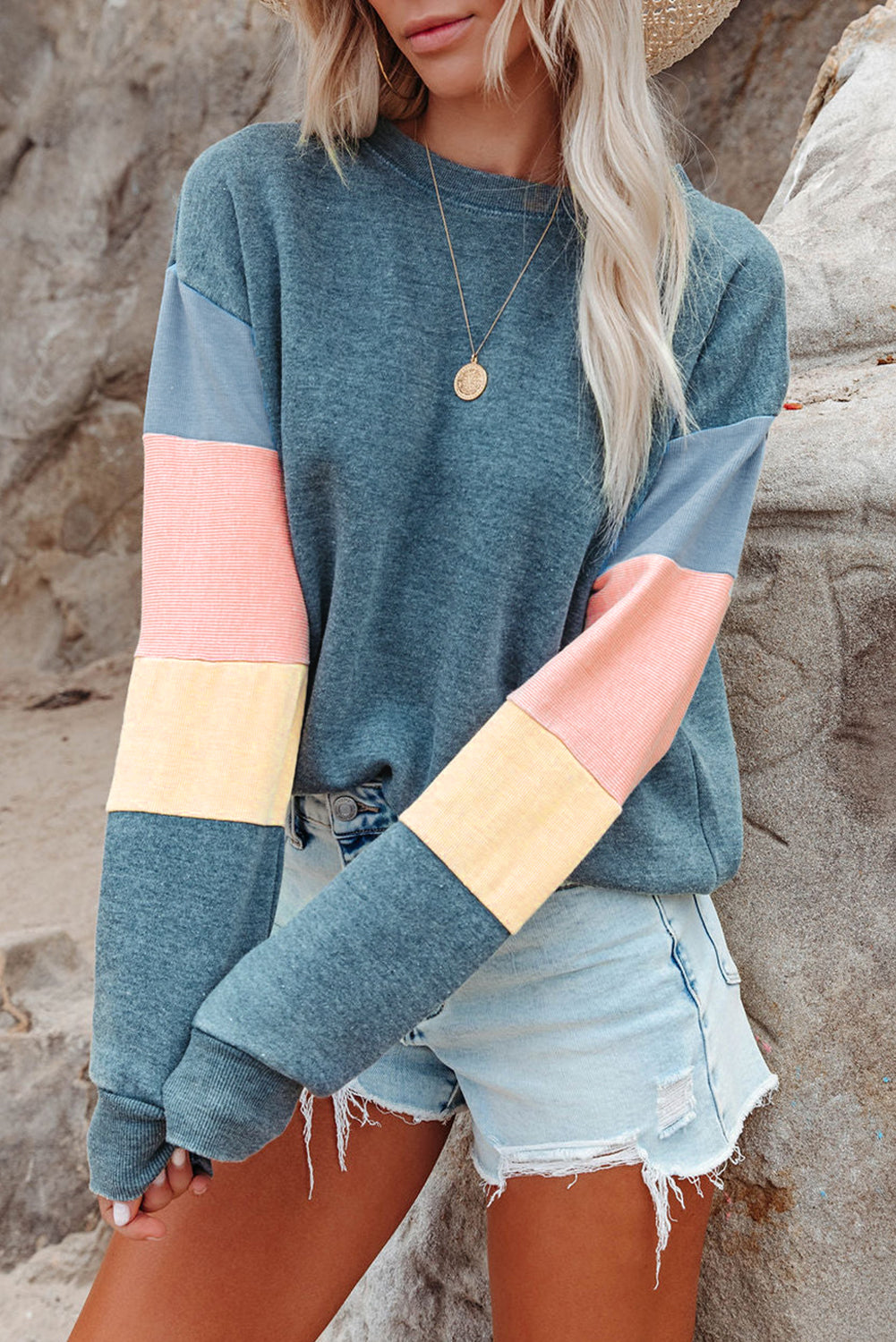 A rear view of a person with wavy hair, dressed in a Blue Colorblock Long Sleeve Pullover Sweatshirt and light blue jeans, hands resting on their hips. Perfect for winter fashion, this versatile piece is an ideal addition to any wardrobe.